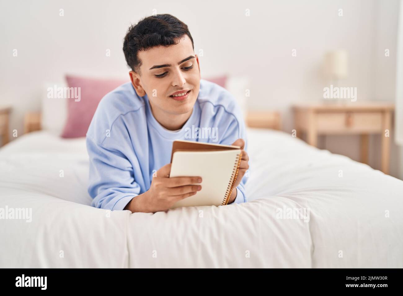 Young non binary man writing on notebook lying on bed Stock Photo - Alamy