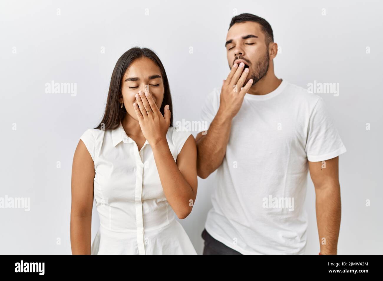 Young interracial couple standing together in love over isolated background bored yawning tired covering mouth with hand. restless and sleepiness. Stock Photo