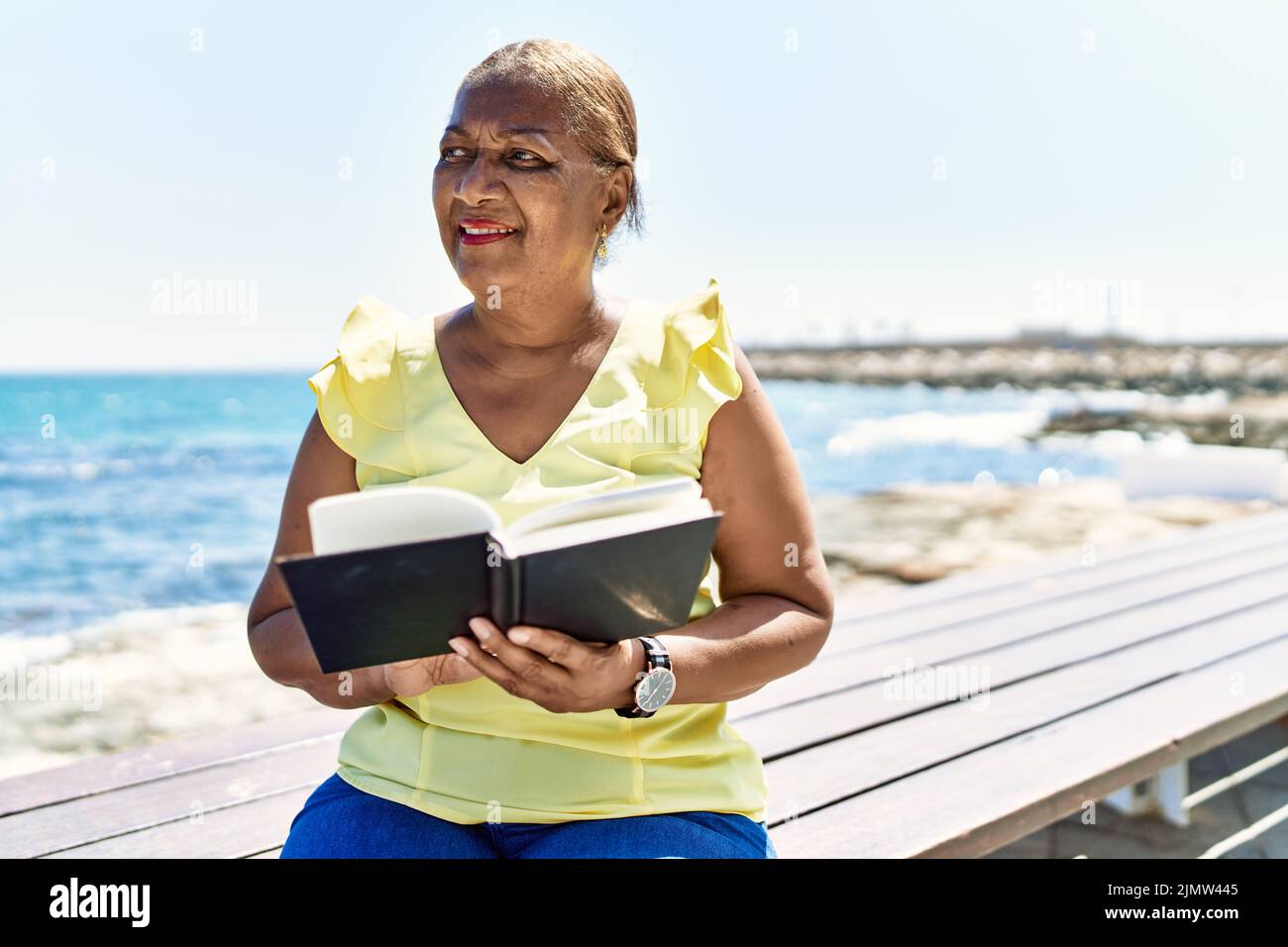 Senior african american woman reading book sitting on the bench at the ...