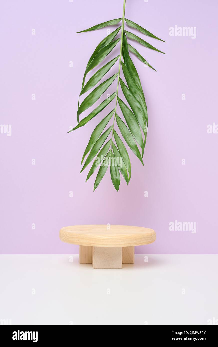 Stage for displaying products, cosmetics with a round wooden podium and a green palm leaf. Stock Photo
