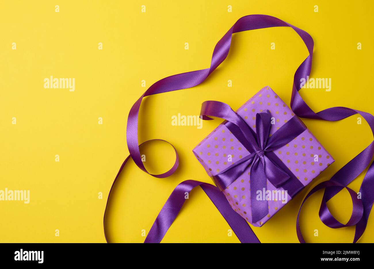 Wrapped boxes in gift purple paper and silk ribbon on a yellow background, top view. Congratulations and surprise Stock Photo