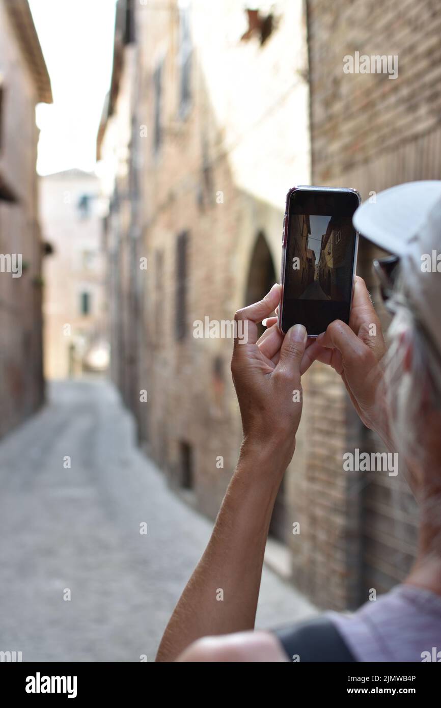 female tourist using cell phone to take pictures in old town of Amandola, Italy Stock Photo