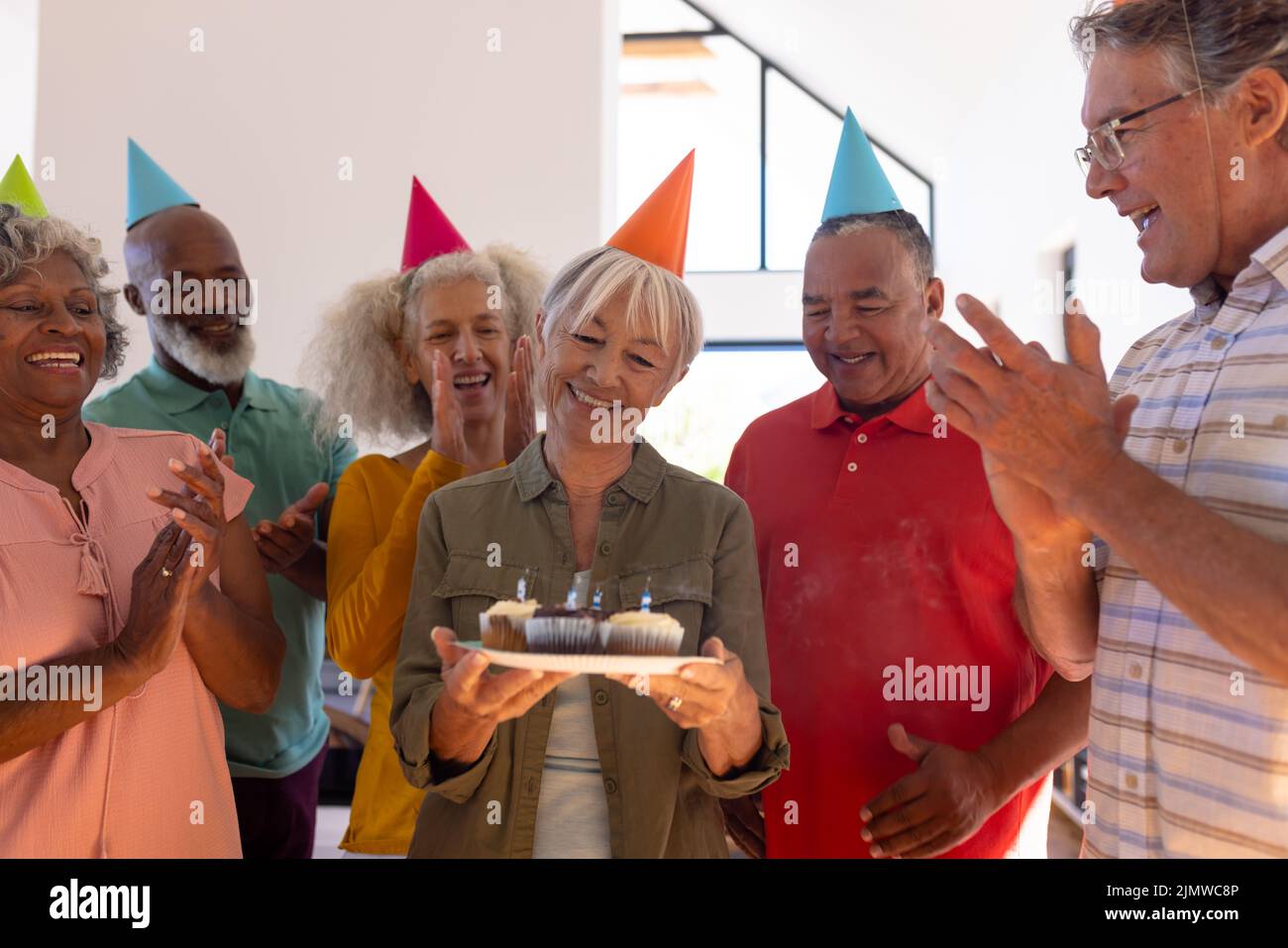 Multiracial friends clapping and singing for happy senior woman holding birthday cupcakes Stock Photo