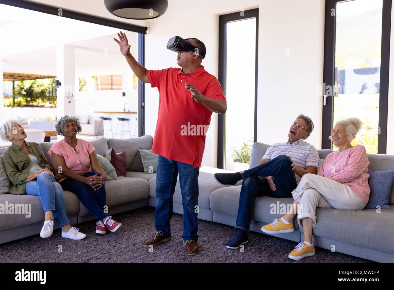 Multiracial friends looking at man using virtual reality simulator while sitting in retirement home Stock Photo