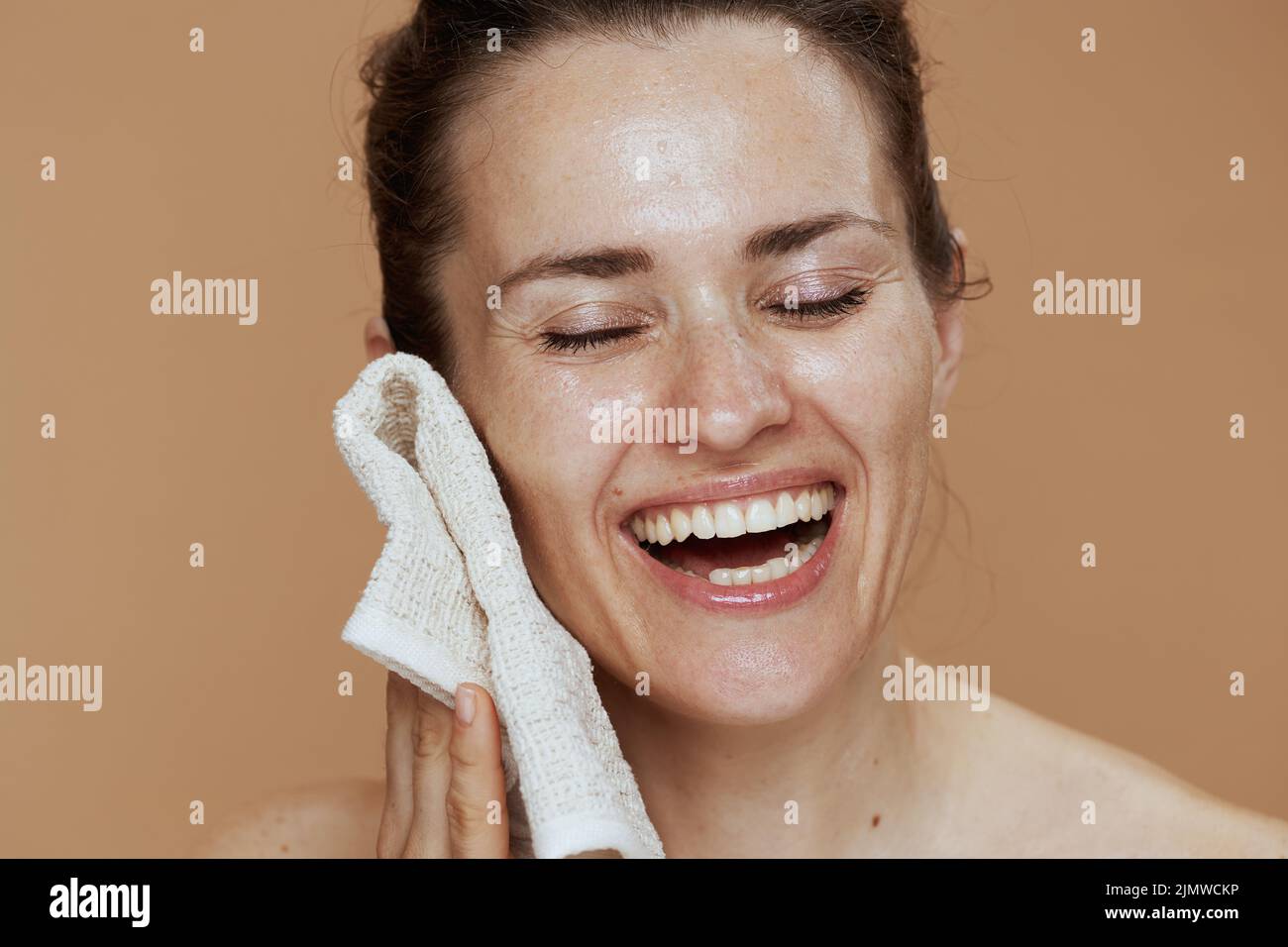 happy middle aged woman with towel washing face on beige background