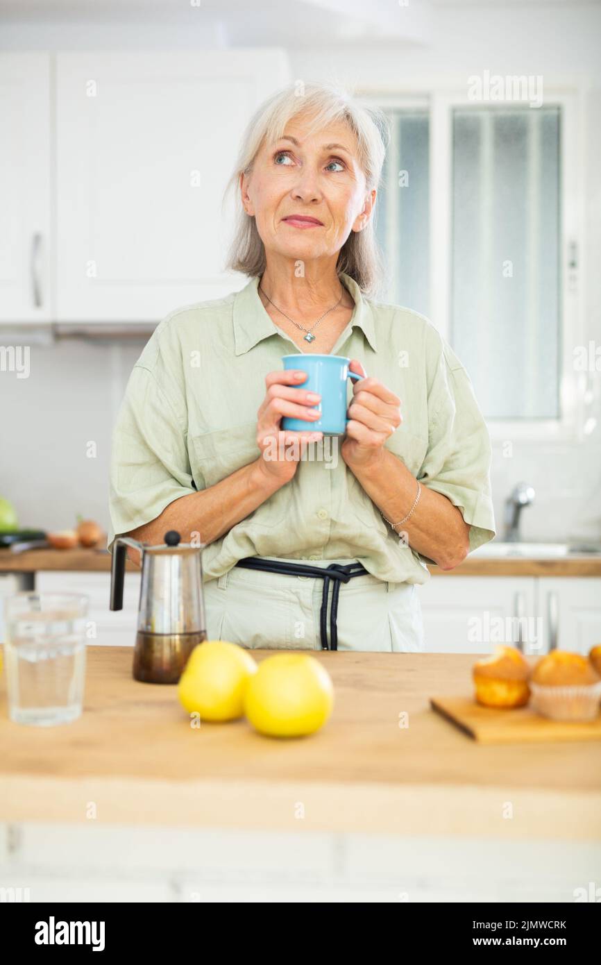 Positive old woman drinking coffee in kitchen at home Stock Photo Alamy