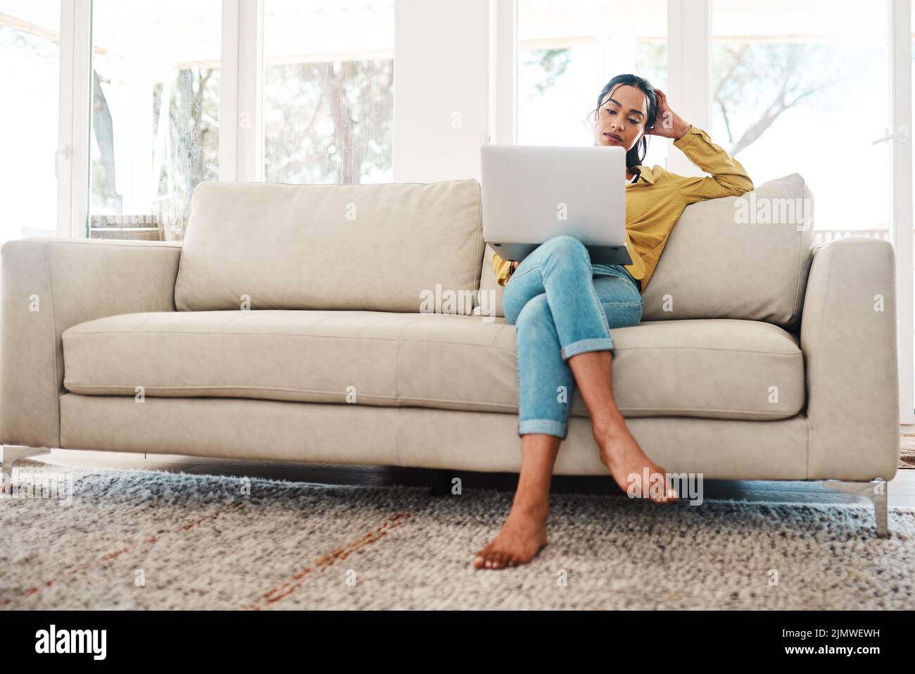 Trying to decide which blog will attract more followers. Full length shot of an attractive young businesswoman sitting on her couch and blogging from Stock Photo