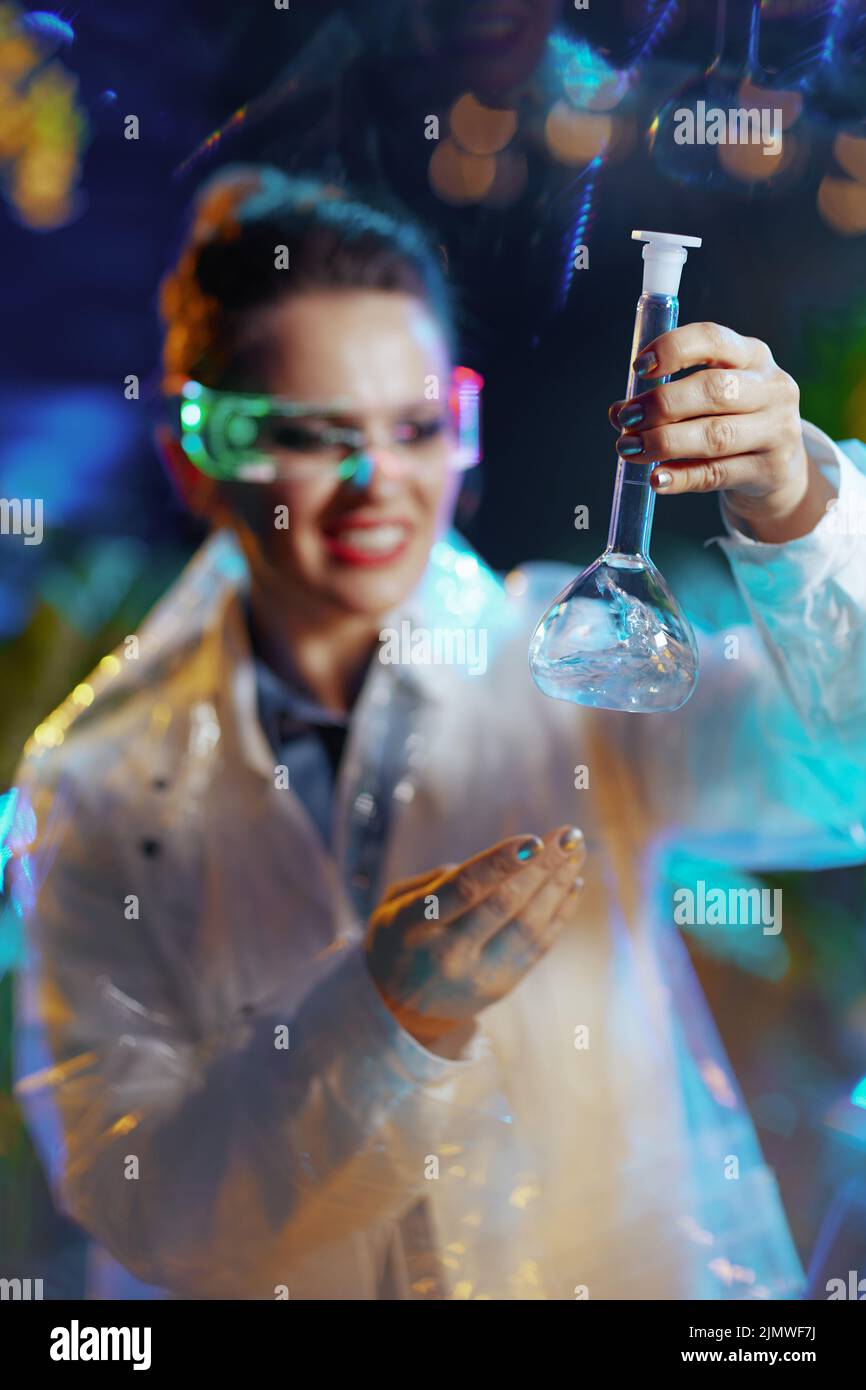 Closeup on smiling scientist woman in lab coat with flask and futuristic goggles in virtual reality. Stock Photo