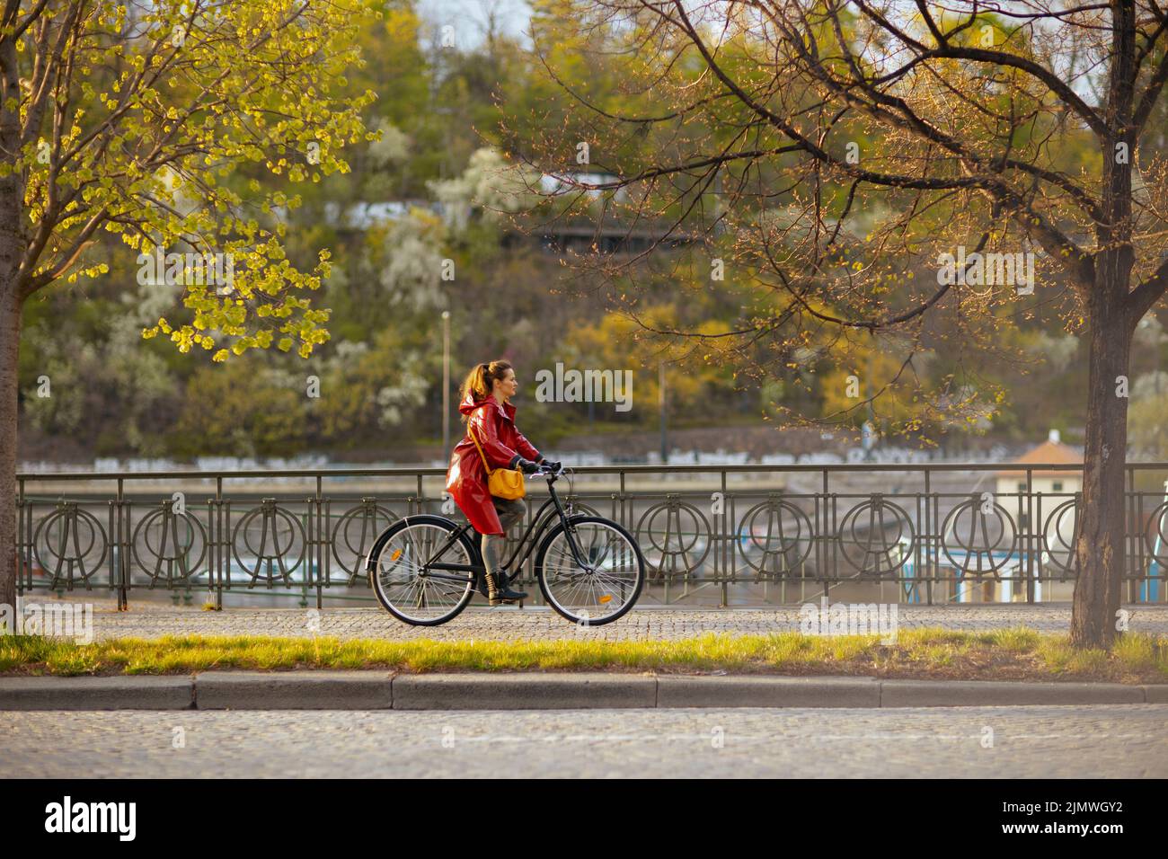 elegant female in red rain coat outdoors on the city street riding ...