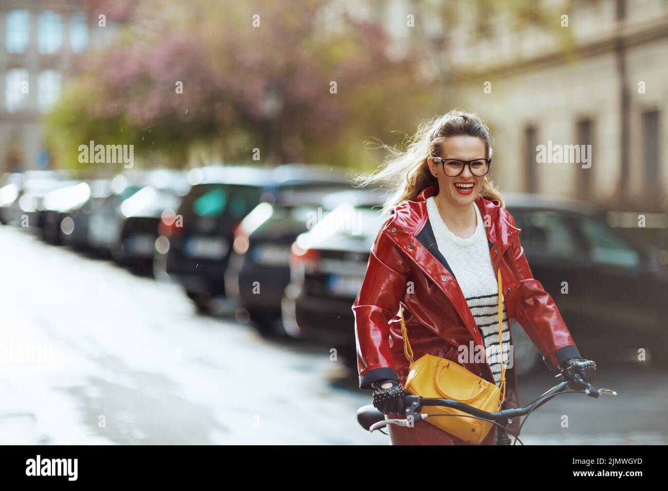 happy stylish middle aged woman in red rain coat outside on the city ...