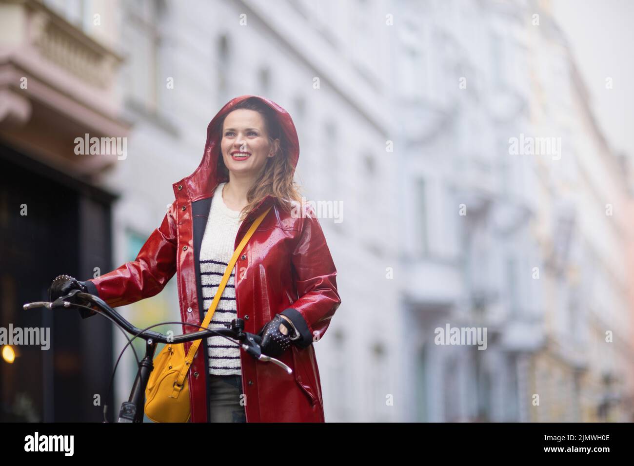 happy elegant woman in red rain coat with bicycle in the rain outside ...