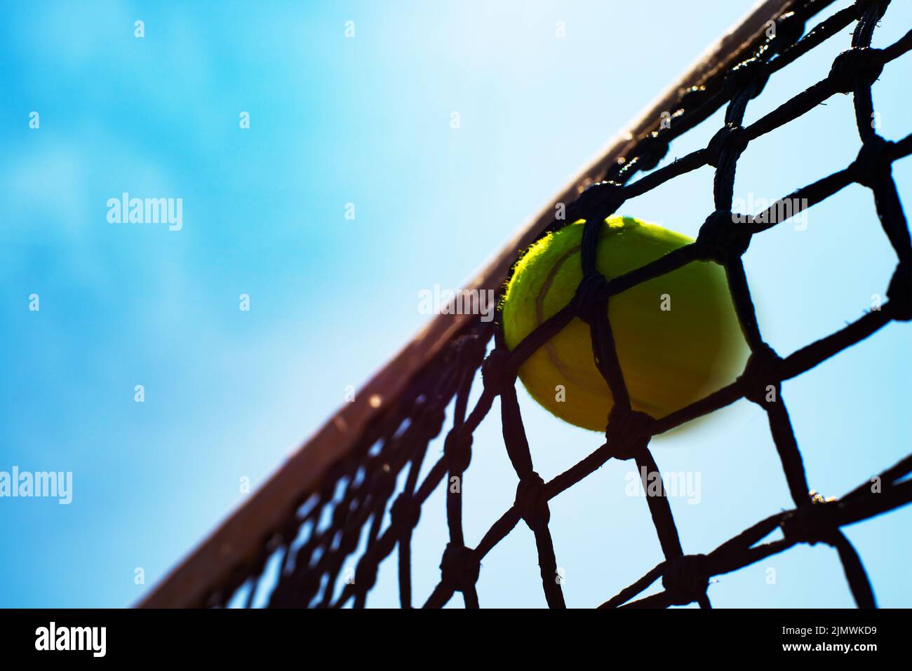 Yellow tennis ball hits in the net during game. Blue sky at background