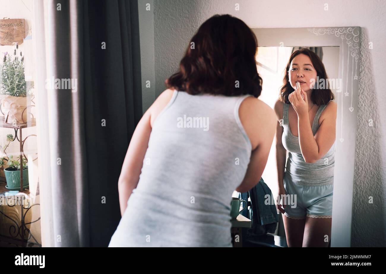 Lets see how my lips look in this. an attractive young woman applying lipstick while standing in front of the mirror in her bedroom at home. Stock Photo