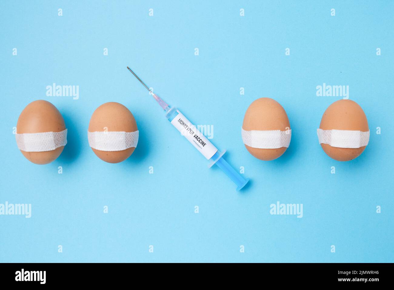 flatlay with monkeypox vaccine syringe and vaccinated eggs with medical patch on blue background. Stock Photo
