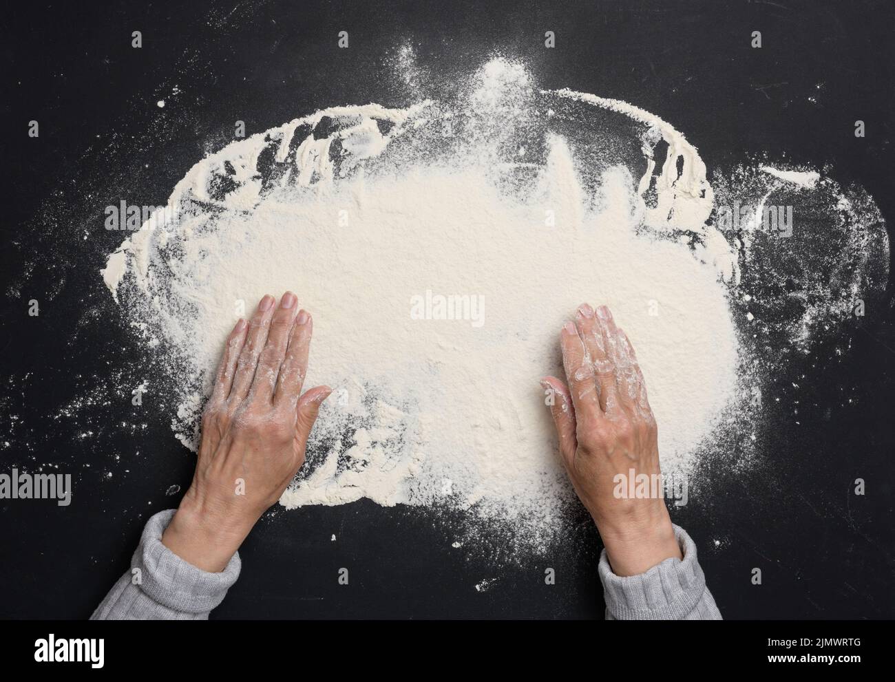 Sifted white wheat flour on a black table and two female hands, top view. cooking at home Stock Photo