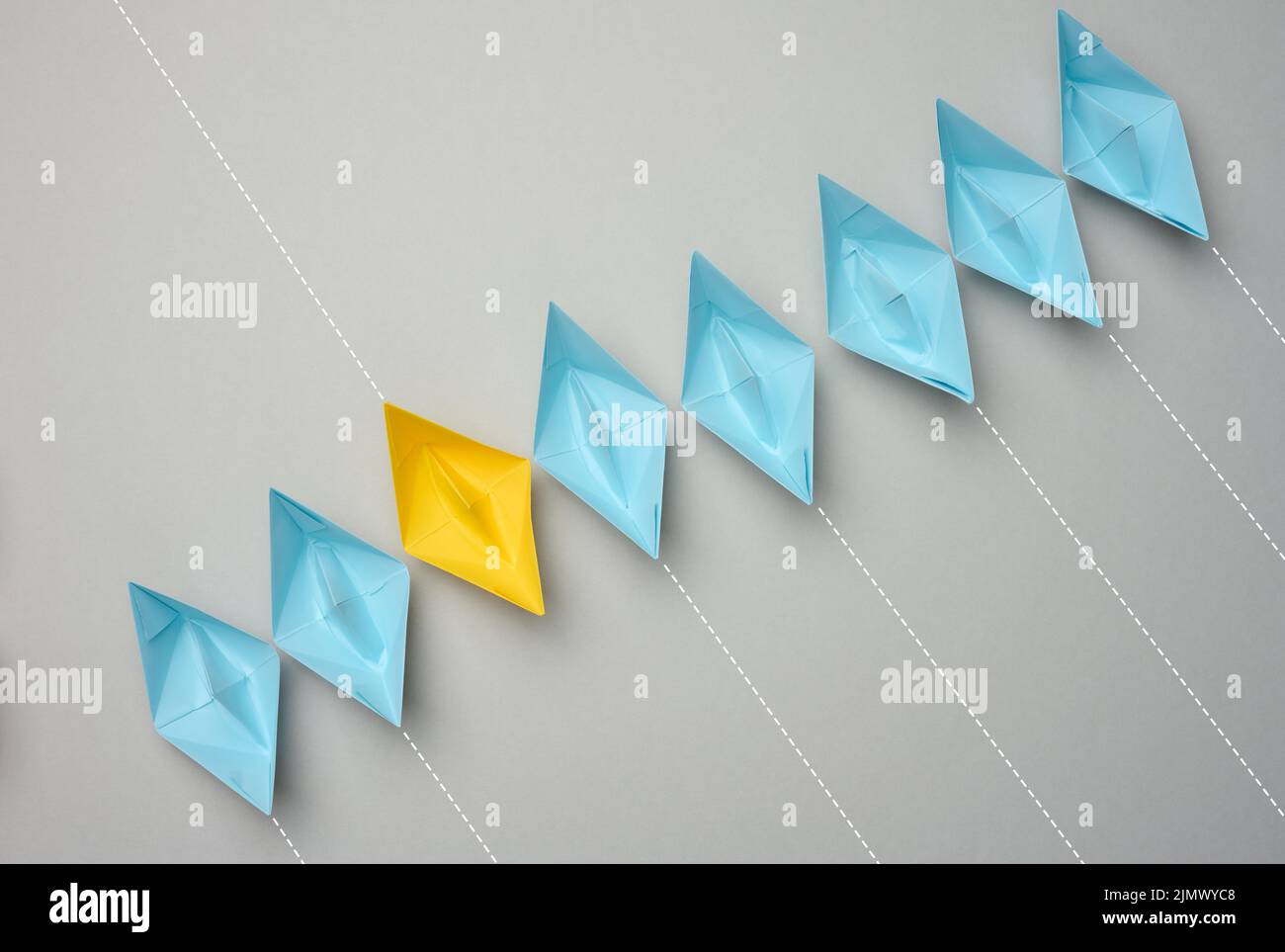 A row of paper boats on a gray background, yellow is moving in the opposite direction Stock Photo