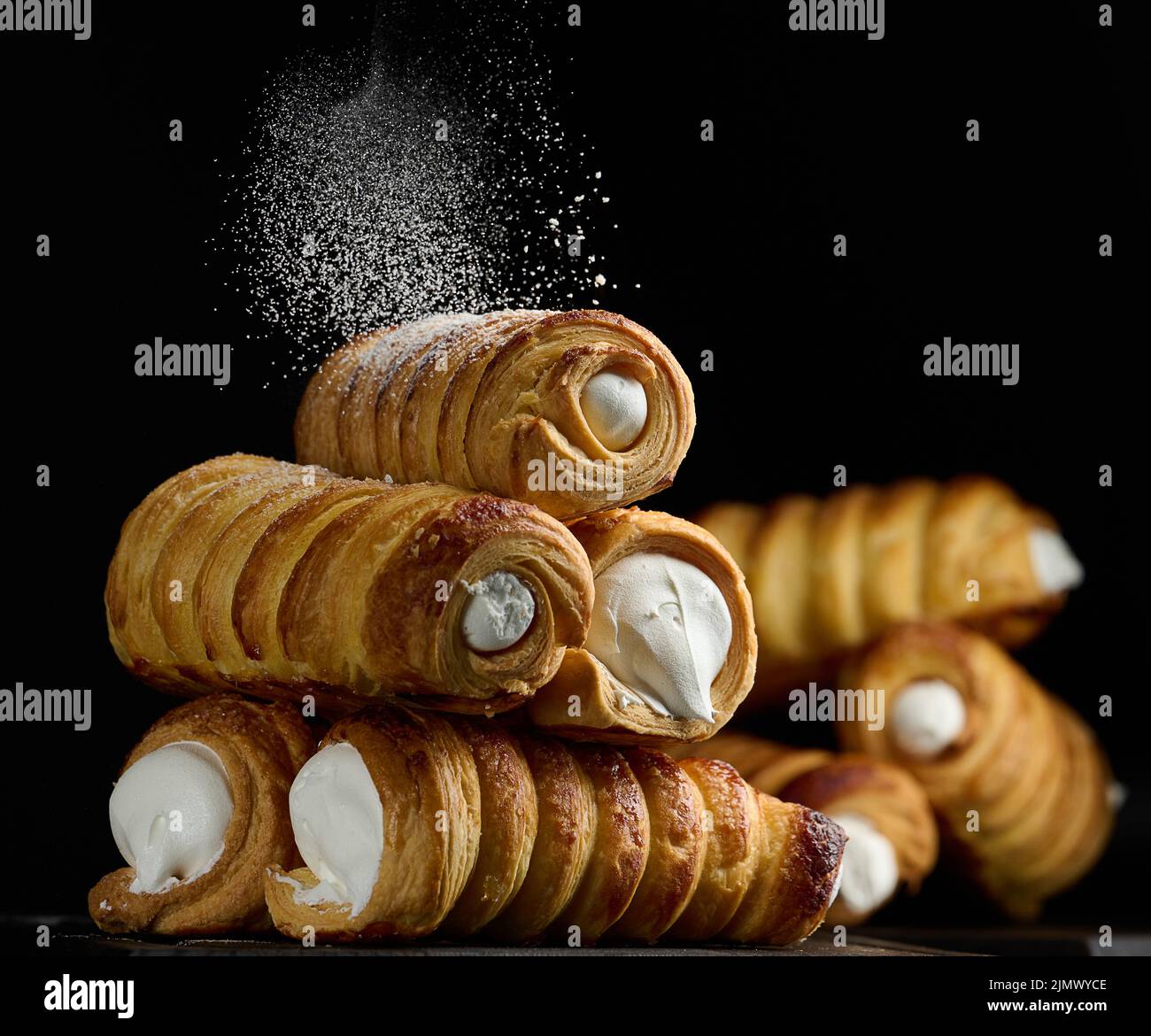 Baked tubules filled with whipped egg whites cream on a black wooden kitchen board Stock Photo