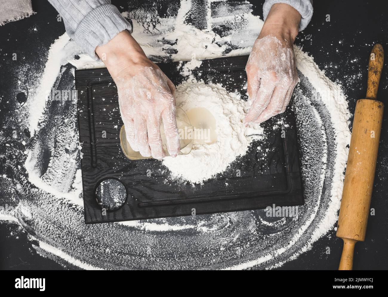 Two female hands knead the dough from white wheat flour on a black table, top view Stock Photo