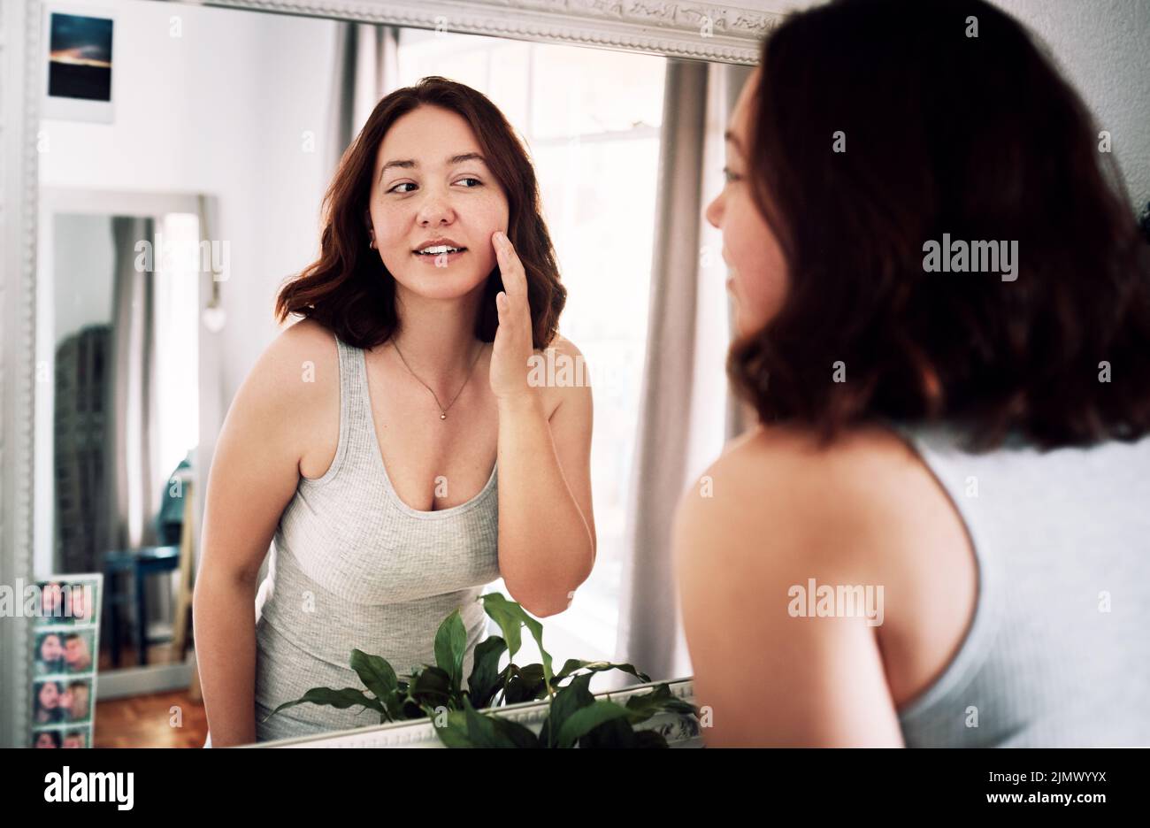 Everything looks so smooth. an attractive young woman inspecting her face while standing in front of the mirror in her bedroom at home. Stock Photo