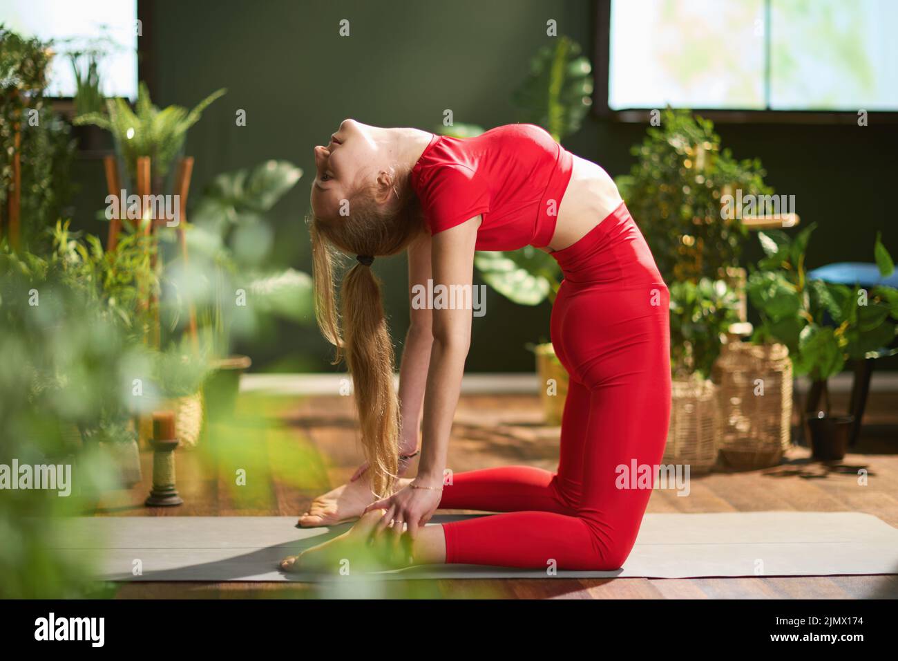 modern woman in red fitness clothes with yoga mat doing yoga at modern green home. Stock Photo