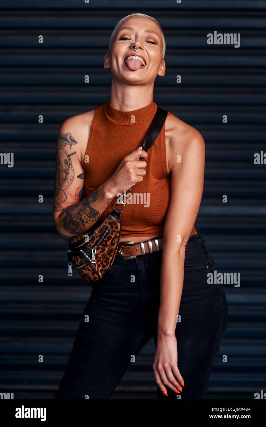 Im so much fun. an attractive young woman sticking out her tongue while standing against a dark background. Stock Photo