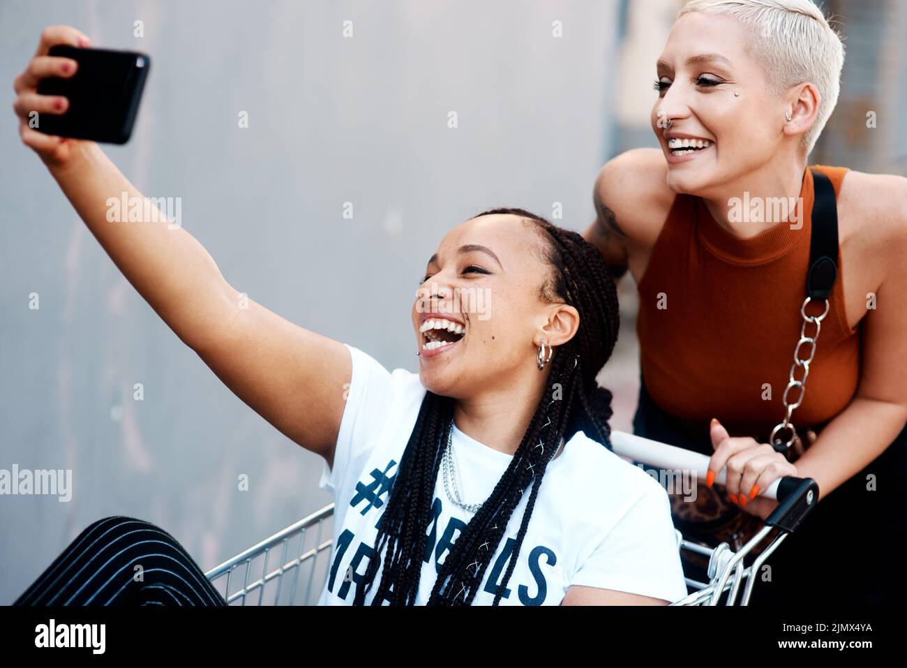 Happy would be an understatement. two cheerful young girlfriends taking a selfie while playing around with a shopping cart outdoors. Stock Photo