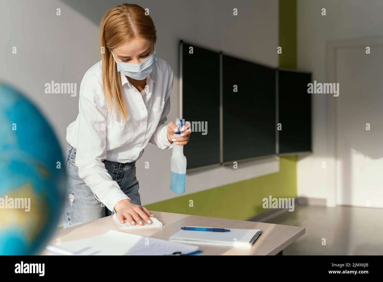 Female teacher disinfecting her desk classroom Stock Photo