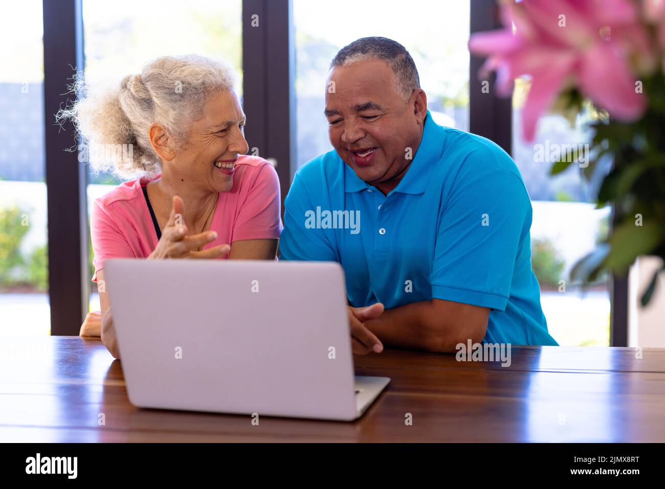 Happy biracial senior man and caucasian woman watching video over laptop while sitting at table Stock Photo