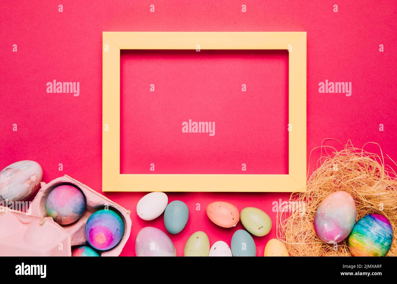 Empty yellow frame with colorful easter eggs pink background Stock Photo