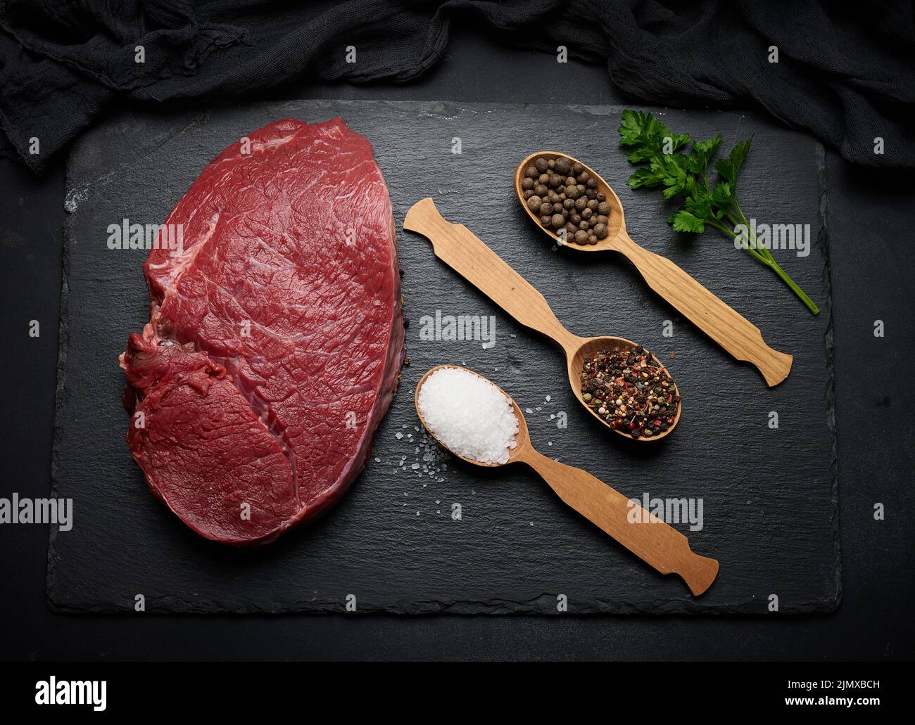 Raw beef tenderloin lies on a wooden cutting board on a black table, top view Stock Photo