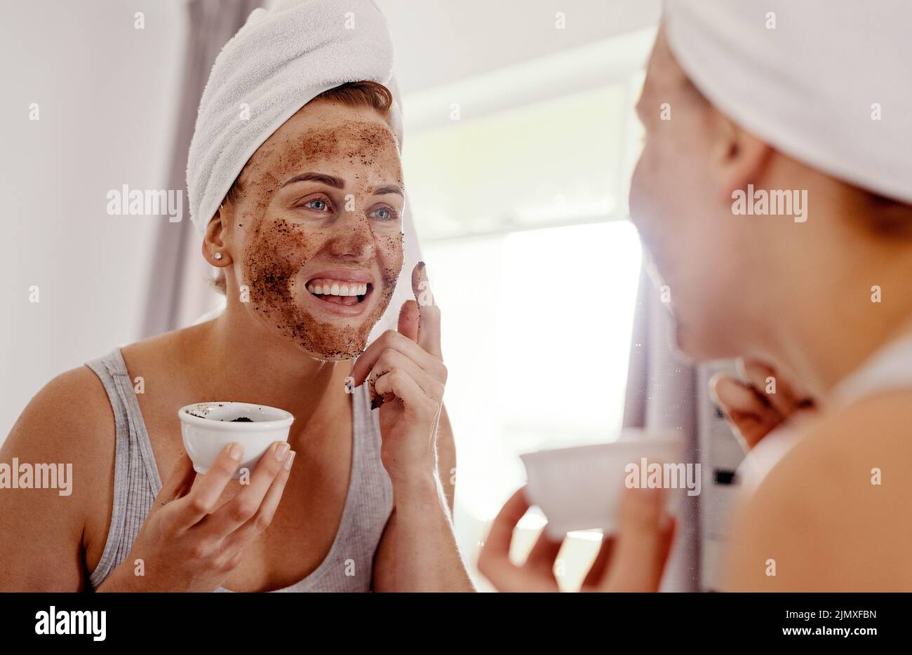 Im so excited about this new routine. an attractive young woman applying a coffee mask on her face while standing in front of the mirror in her Stock Photo