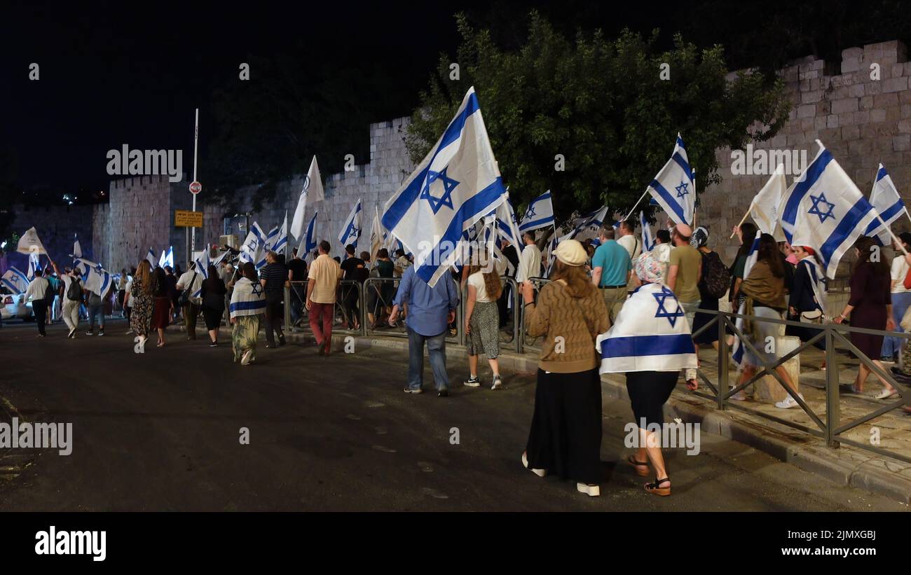 Religious Jews hold Israeli flags as they march along the walls of the old city during the 'Sivuv Shaarim' (Circling of the Gates) celebration around the gates of the Temple Mount, on the Jewish feast of Tisha B'Av on August 6, 2022 in Jerusalem, Israel. Jews around the world read today from the Book of Lamentations, marking the beginning of Tisha B'Av, the annual fasting day commemorating the destruction of the First and Second Temples in Jerusalem Stock Photo