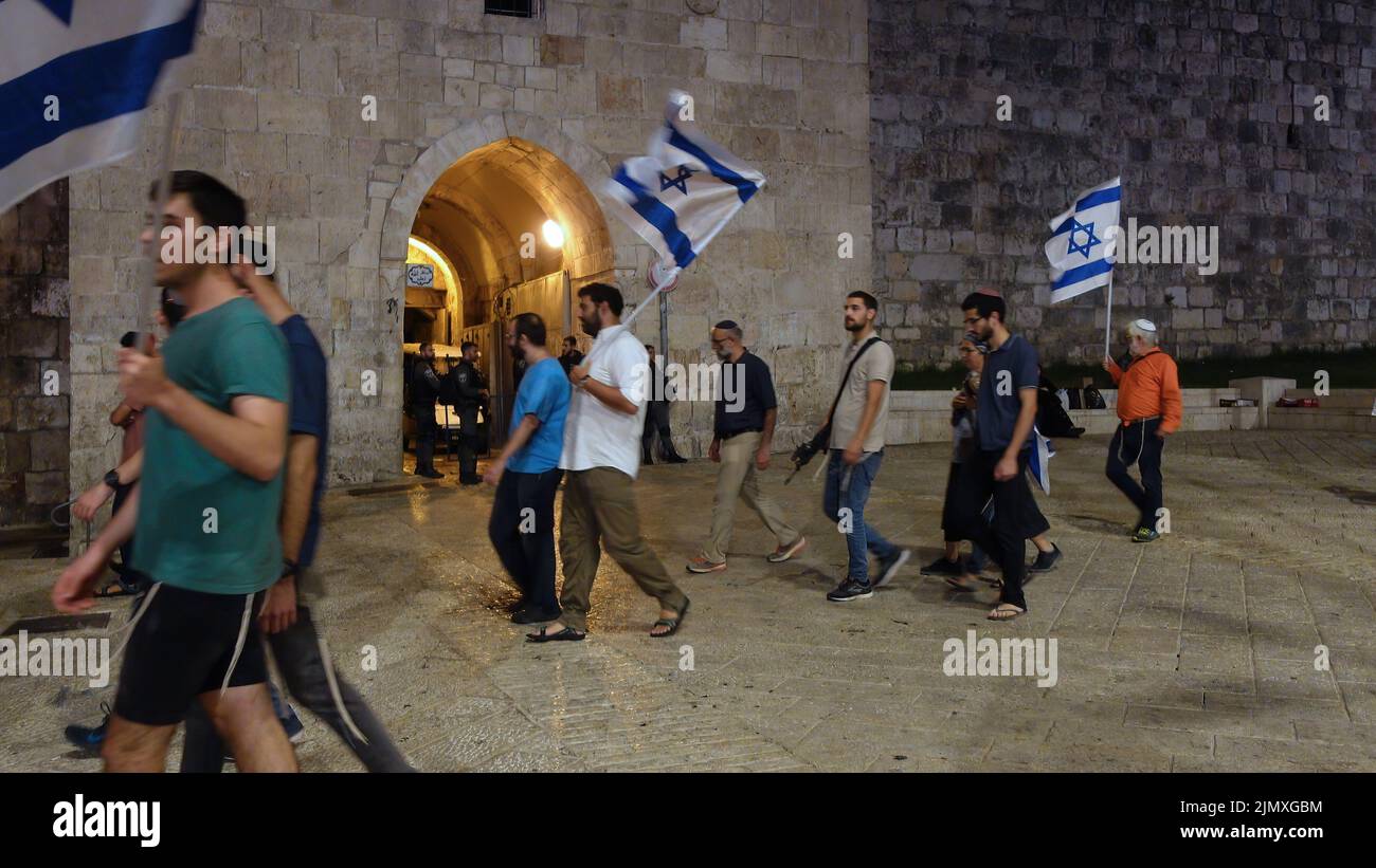 Religious Jews hold Israeli flags as they walk past Herod's gate also Bab el Zahra during the 'Sivuv Shaarim' (Circling of the Gates) celebration around the gates of the Temple Mount, on the Jewish feast of Tisha B'Av on August 6, 2022 in Jerusalem, Israel. Jews around the world read today from the Book of Lamentations, marking the beginning of Tisha B'Av, the annual fasting day commemorating the destruction of the First and Second Temples in Jerusalem. Stock Photo