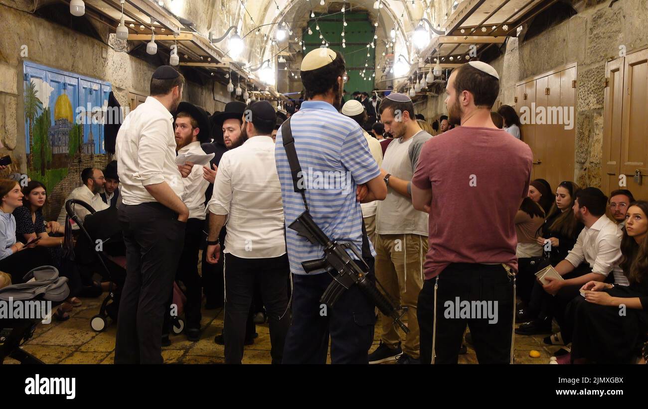 An armed religious Jew stands with other Jews before prayer at Bab al-Qattanin gate, which leads to the Temple Mount in the Muslim Quarter, on the Jewish feast of Tisha B'Av on August 6, 2022 in Jerusalem, Israel. Jews around the world read today from the Book of Lamentations, marking the beginning of Tisha B'Av, the annual fasting day commemorating the destruction of the First and Second Temples in Jerusalem Stock Photo