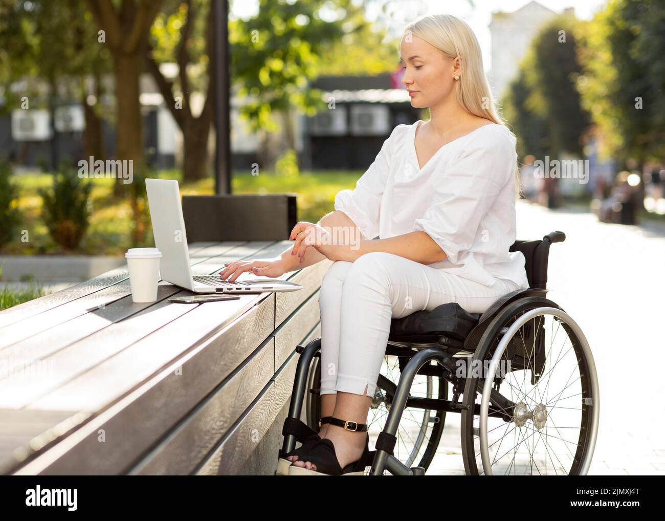 Woman wheelchair using laptop outdoors Stock Photo