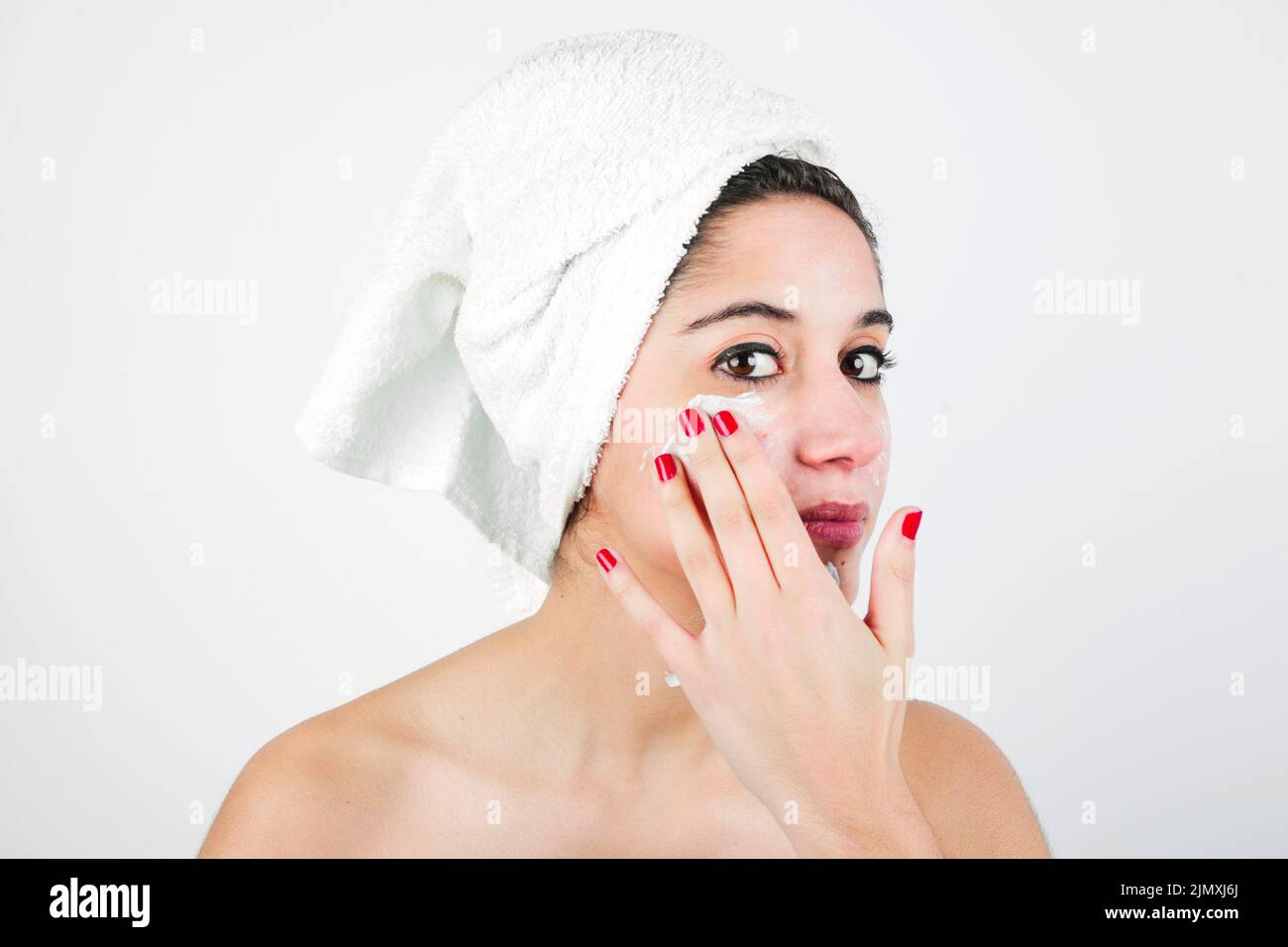 Young woman applying cream face with white towel her head Stock Photo