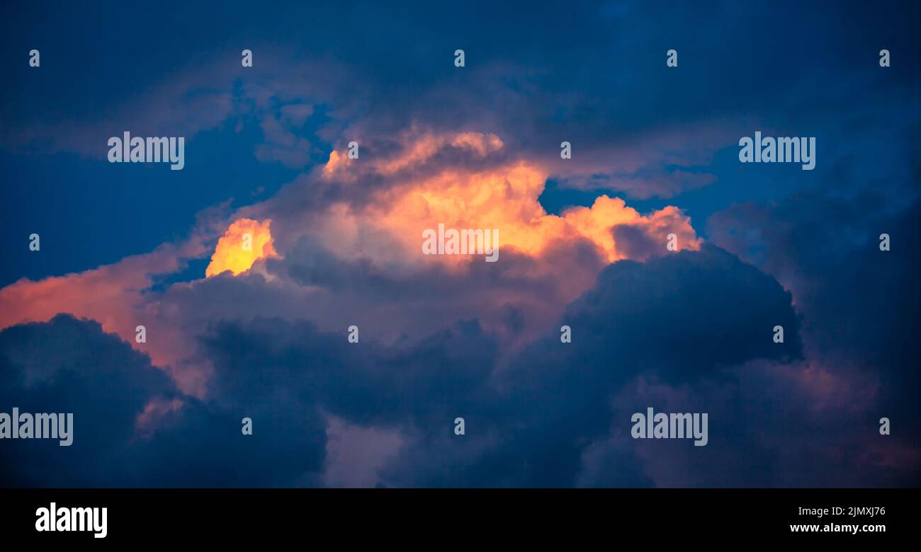 Orange clouds in the center of the dark blue, illuminated by the sun at sunset. Abstract sky at sunset. Stock Photo
