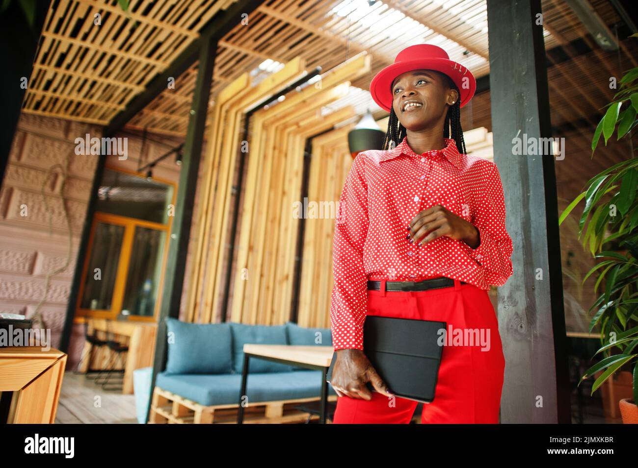 Pretty braids business african american lady bright bossy person friendly wear office red shirt, hat and trousers, hold tablet o Stock Photo