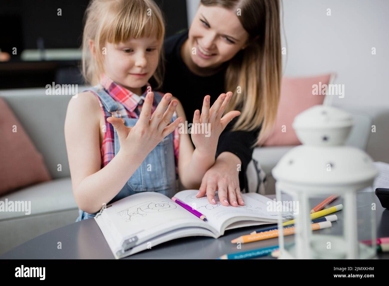 Girl looking hands while doing homework with mom Stock Photo