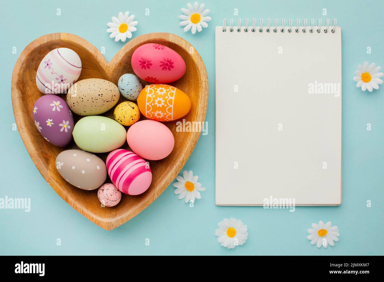 Top view colorful easter eggs heart shaped plate with notebook flowers Stock Photo