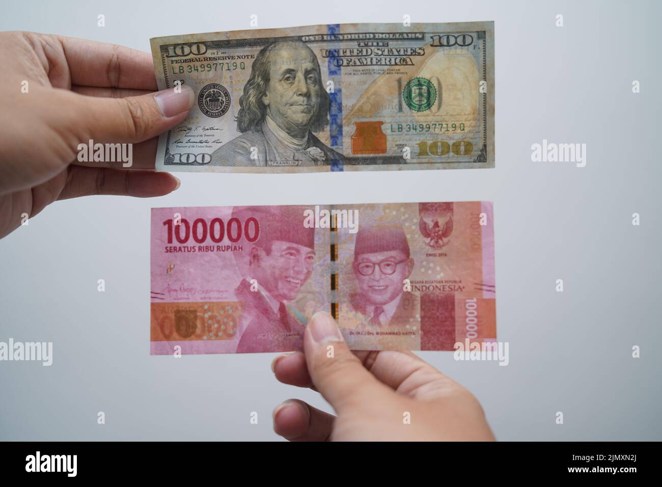 hand holding one hundred thousand rupiah and one hundred dollars isolated on white background Stock Photo