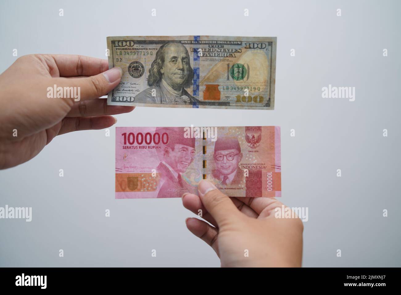hand holding one hundred thousand rupiah and one hundred dollars isolated on white background Stock Photo