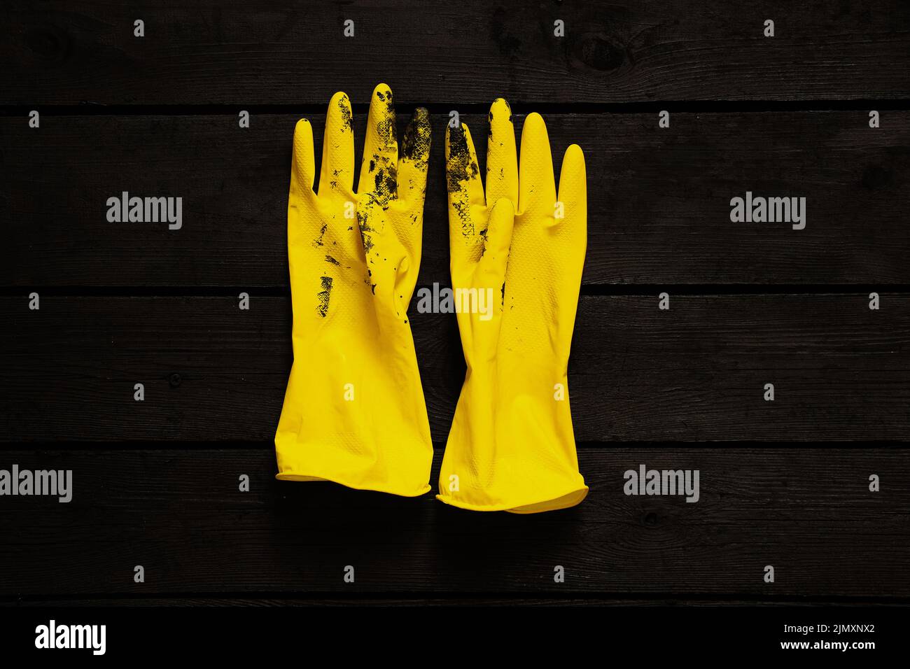 yellow rubber gloves in black paint on a black wooden floor, gloves in
