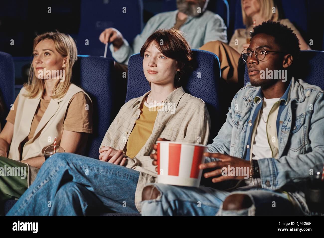 Group of ethnically diverse people sitting in modern cinema with blue