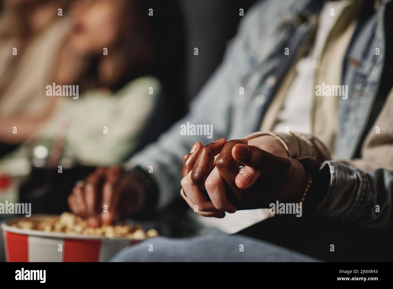 Selective focus of unrecognizable ethnically diverse couple holding hands while watching film at cinema Stock Photo