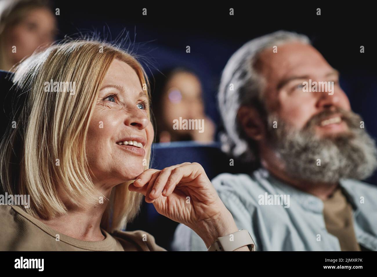 Selective focus shot of mature Caucasian woman with blond haor spending spare time watching film at cinema Stock Photo