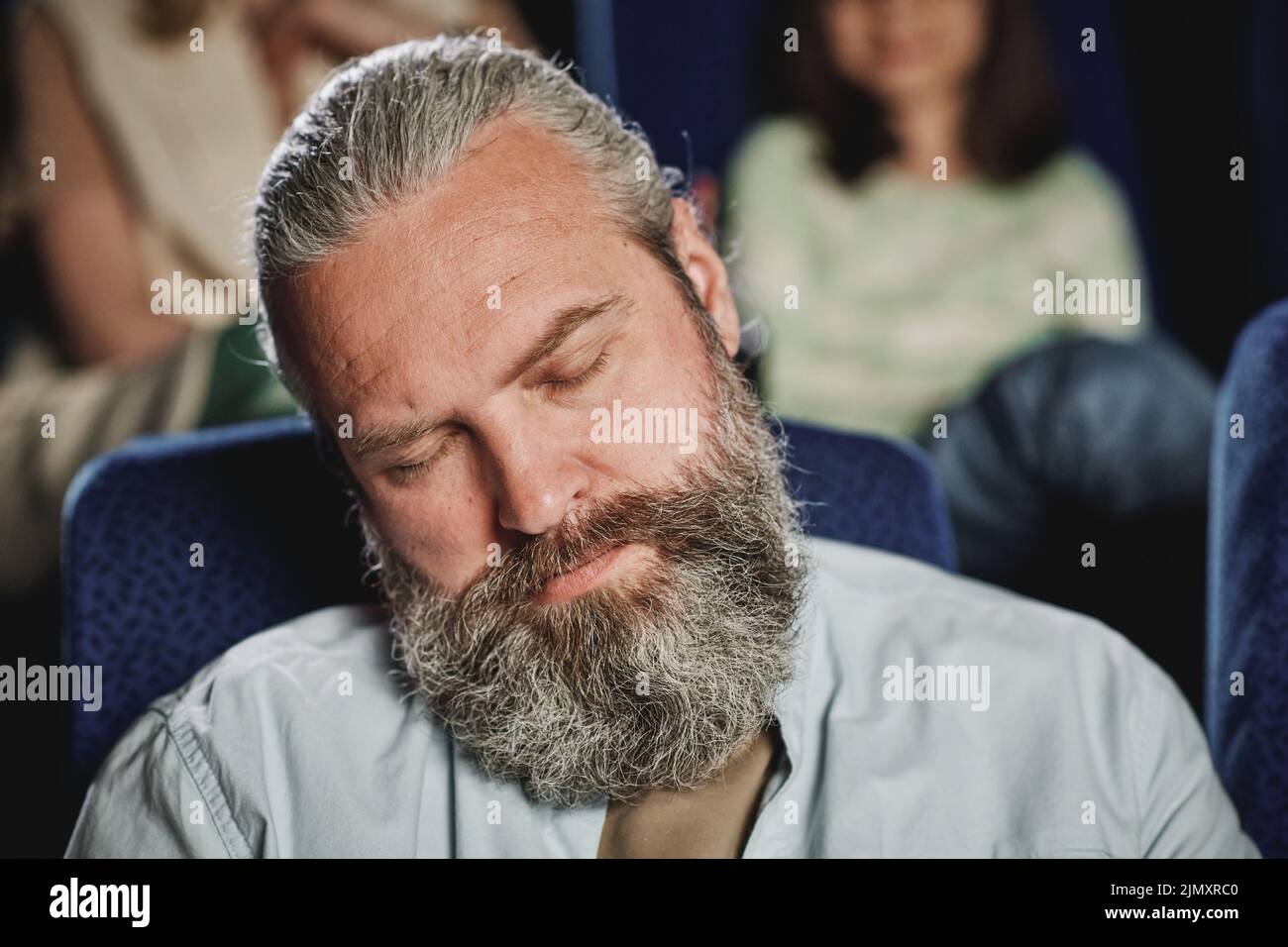 Selective focus close-up of mature Caucasian man falling asleep while watching boring movie at cinema Stock Photo