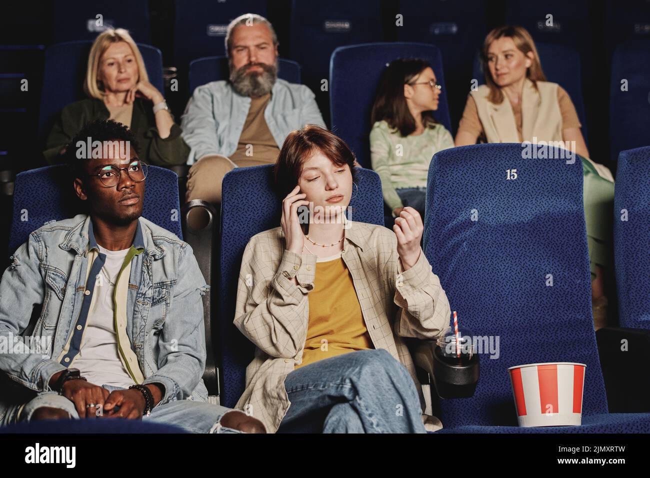Young gen Z Caucasian woman talking on phone while watching movie at cinema distracting other people Stock Photo