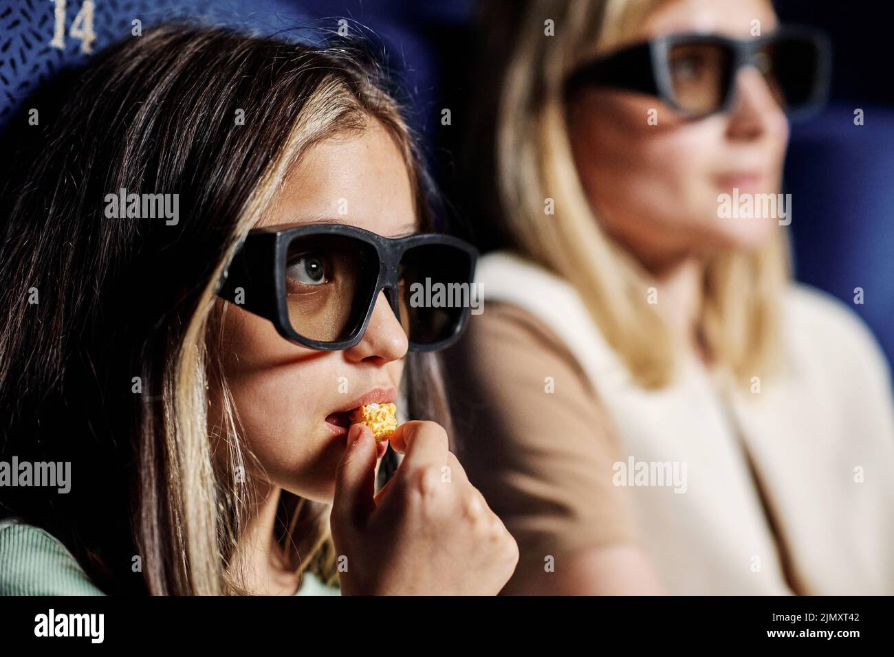 Selective focus portrait of preteen girl wearing polarized 3D glasses watching movie and eating sweet popcorn at cinema Stock Photo