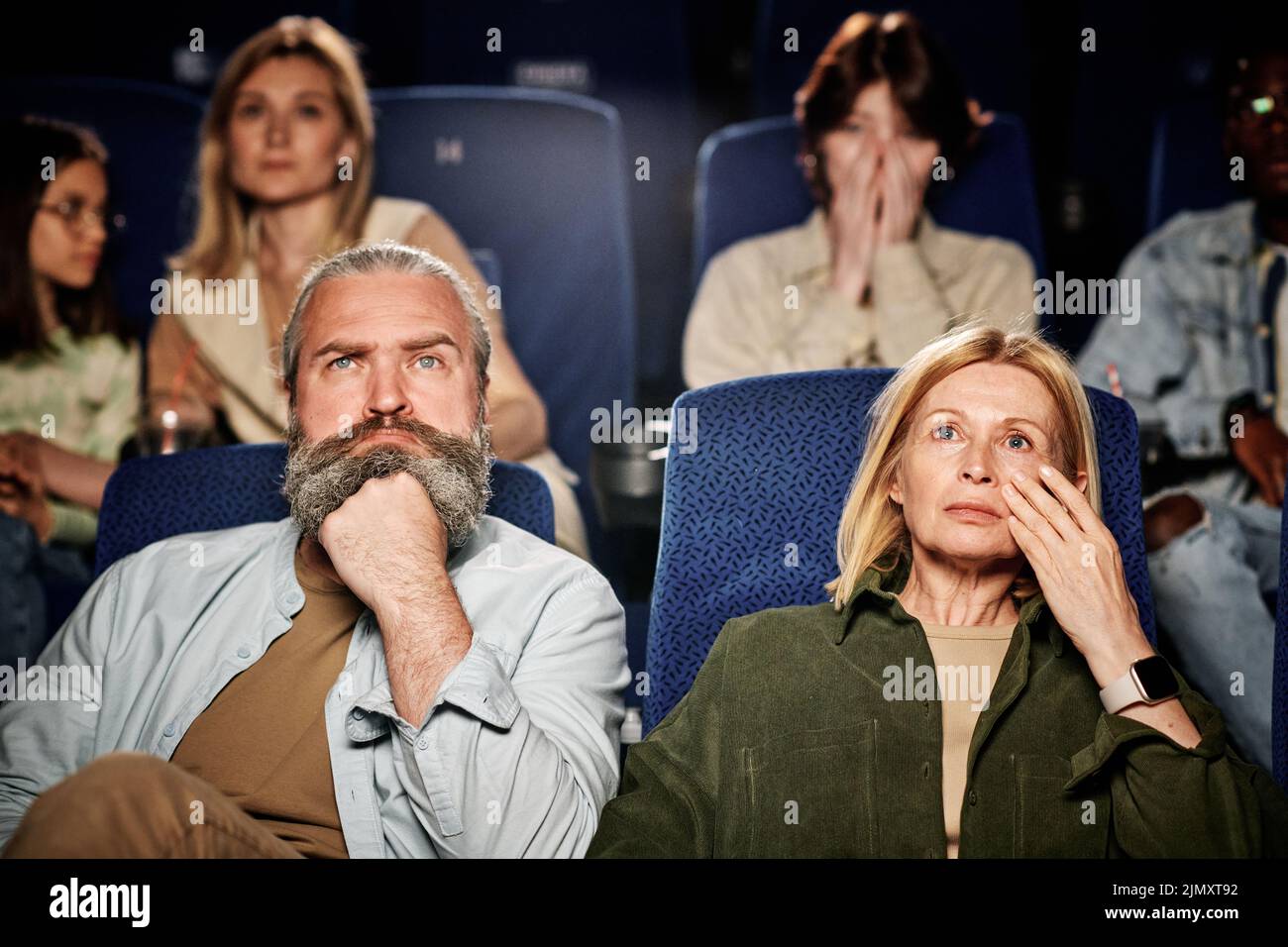 Selective focus of mature Caucasian man and woman watching drama movie at cinema, woman wiping tears with hand Stock Photo